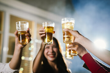 Group of friends raising glasses of beer together in a cheerful toast, celebrating with bright bokeh lights in the background.