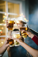 Group of friends raising glasses of beer together in a cheerful toast, celebrating with bright bokeh lights in the background.