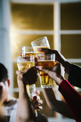 Group of friends raising glasses of beer together in a cheerful toast, celebrating with bright bokeh lights in the background.