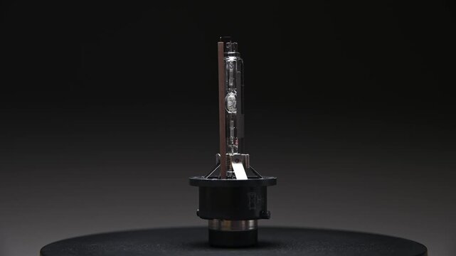 A close-up of a xenon headlight bulb. The rotating part is on a gradient gray background.
