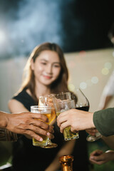 Group of friends raising glasses of beer together in a cheerful toast, celebrating with bright bokeh lights in the background.