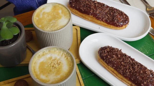 Fresh sweet eclairs cakes with cream cheese and chocolate chips with coffee on the table in a cozy cafe. High quality 4k footage