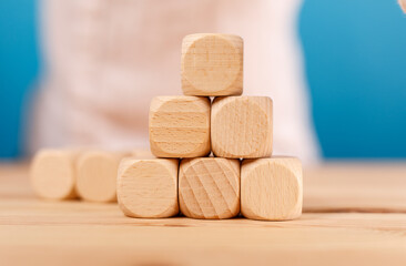 Close up of wooden cubes forming a pyramid on a wooden table, with a blue background, conveying concepts like building, construction, and succes
