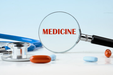 A stethoscope and pills rest on a white surface, with a magnifying glass showing the word MEDICINE, representing health and discoveries