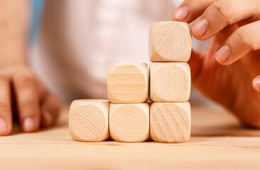 A hand carefully placing a wooden cube on top of a stack of other wooden cubes.  Concept of building, creation, or construction.