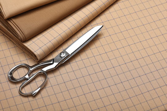 Tailoring shears resting on folded camel wool fabric with a blue windowpane check pattern, symbolizing bespoke garment making for autumn, winter season. - Powered by Adobe