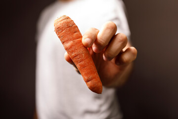 A person's hand holding a fresh, raw carrot against a dark background, showcasing the healthy vegetable. Perfect for food and healthy eating con
