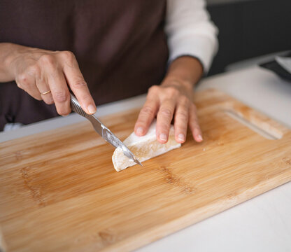 Woman's hands cutting a piece of cheese on a wooden cutting board, preparing food - Powered by Adobe