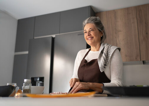 Happy senior woman wearing an apron preparing food on a cutting board at home - Powered by Adobe