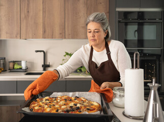 Senior woman removing homemade pizza from oven