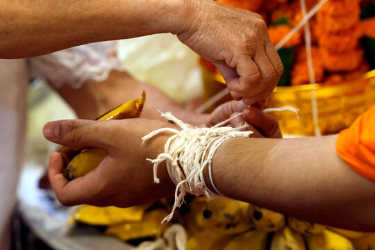 Buddhist ceremony at Wat May Souvannapoumaram temple. Monk ties blessed cotton bracetet ( Sai-sin) around a wrist. Luang Prabang. Laos.
