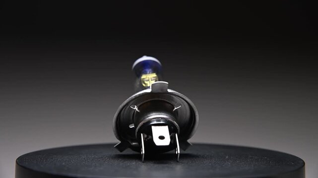 A halogen headlight h4 bulb for a car. This spare part for ambient lighting rotates on a black gradient background.