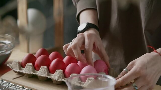Close up of hands of unrecognizable woman putting freshly colored red Easter eggs in carton