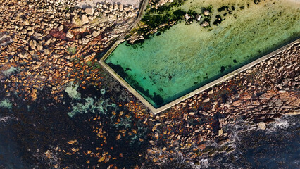 Aerial view of the contrast between the turquoise tidal pool and rugged, rocky coastline creates a stunning visual symphony, Cape Town, Western Cape, South Africa.