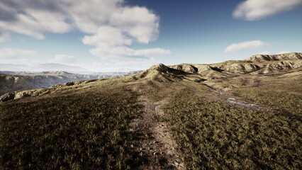 Open fields stretch across the horizon under a clear blue sky. Soft clouds drift above, casting shadows on the rugged terrain. Nature remains undisturbed in this serene setting.