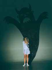 Creative digital artwork. Little girl covering eyes before giant devil shadow on green wall....