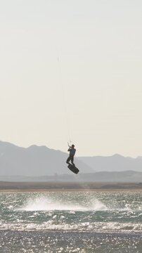 Slow motion vertical video kitesurfer performing high jump megaloop trick at sunset extreme sport action adrenaline ocean waves freedom cinematic epic athlete lifestyle summer training adventure