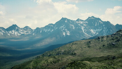 Towering peaks rise dramatically against a soft blue sky, with sunlight casting shadows on lush green hills. This remote wilderness showcases natures beauty and tranquility.