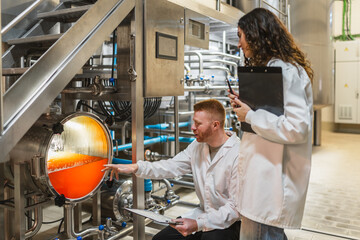 Craft brewery staff in lab coats checking a brewing tank with beer, ensuring quality control and efficient production process