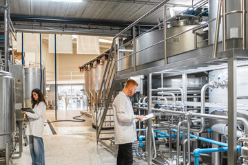 Biotechnologists monitoring industrial machinery and processing tanks in a beverage production facility, ensuring quality control and efficiency