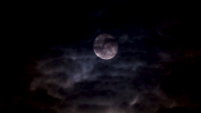 Full moon on a dark cloudy night with clouds flying in front of the moon like in thrillers and horror movies. Dark night sky, black clouds. Real shooting