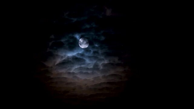 Full moon on a dark cloudy night with clouds flying in front of the moon like in thrillers and horror movies. Dark night sky, black clouds. Real shooting