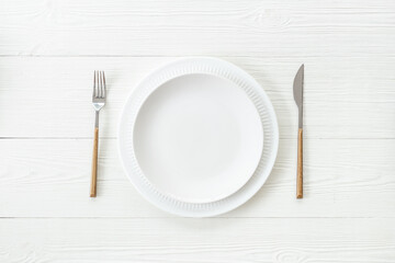 Top view of minimalistic table setting with empty plate and cutlery on white wooden background,...