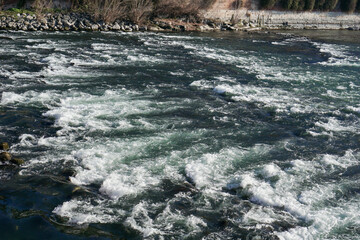 dark river Adisch water rushing over rocks creating white foam and ripples with shoreline visible in the distance concept of river energy, fast currents, water transportation