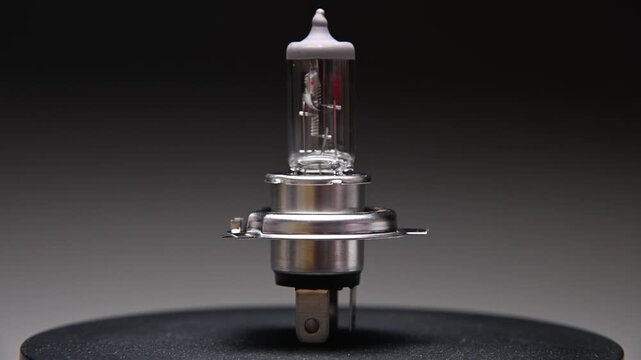 A halogen headlight h4 bulb for a car. This spare part for ambient lighting rotates on a black gradient background.
