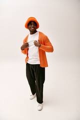 Stylish young man exudes charm in vibrant orange outfit and casual footwear