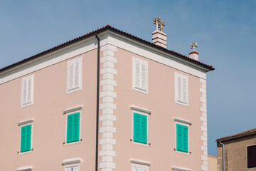 Pastel building in Piran with turquoise shutters and rooftop crosses under clear sky