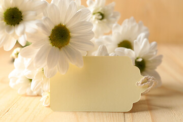 Blank tag and flowers on wooden table, closeup