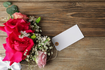 Blank tag and flowers on wooden table, flat lay