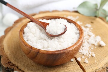Sea salt in bowl, spoon and eucalyptus leaves on table, closeup