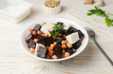 Beet Salad with chickpeas, feta and green sauce with oil and parsley in a white bowl with ingredients on a wooden table. Healthy eating. Horizontal orientation. Selective focus. Top view.