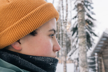 Profile of a young girl wearing a beanie and a scarf, looking at a snowy forest during winter