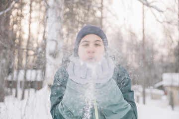 Teenager girl having fun blowing snow in his hands in a winter forest landscape