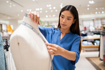 Fashion designer adjusts a white dress form in a bright store studio.