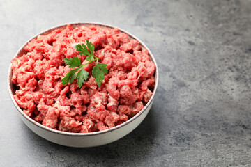 Raw minced meat with parsley on grey table, closeup. Space for text