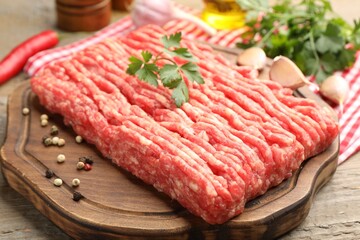 Raw minced meat with parsley and spices on wooden table, closeup
