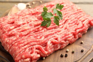 Raw minced meat with parsley and spices on wooden table, closeup