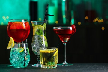Glasses of tasty cocktails on dark table against blurred background, bokeh effect. Space for text