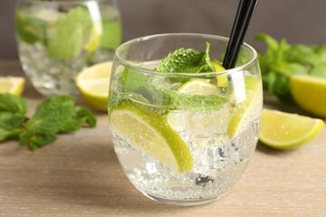 Glasses of tasty cocktails with limes and mint on wooden table, closeup