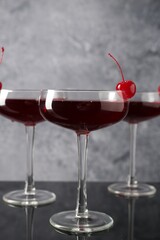 Glasses of tasty cocktails with garnish on mirror surface, closeup