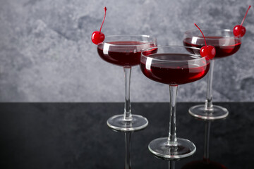 Glasses of tasty cocktails with garnish on mirror surface, closeup