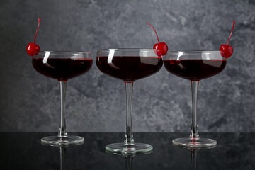 Glasses of tasty cocktails with garnish on mirror surface