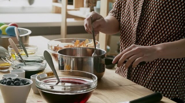 Mid-section shot with side view of unrecognizable woman with spoon mixing onion peels in cooking pot and preparing natural Easter eggs dye