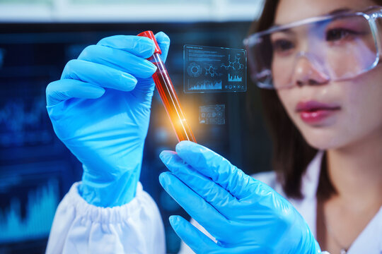 Asian female scientist, wearing blue gloves and safety goggles, closely holds a blood sample test tube where holographic diagnostic data and molecular structures are digitally overlaid.