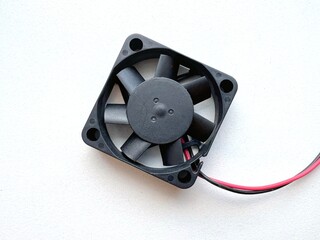Small black cooling fan with red and black wires, isolated on white background, electronic hardware component