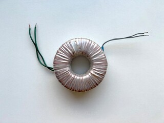 Toroidal transformer with exposed copper wiring and leads on white background, isolated electrical component